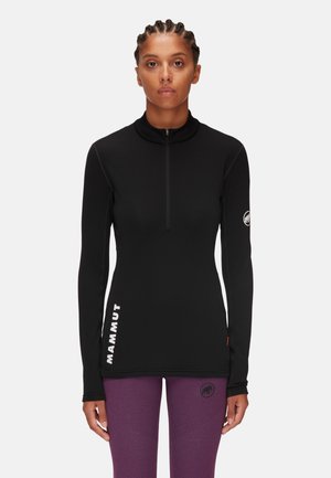 Pull con maniche lunghe nero con colletto alto, presenta una zip a metà lunghezza, dettaglio logo laterale e cuciture a contrasto. Indossato con leggings viola.