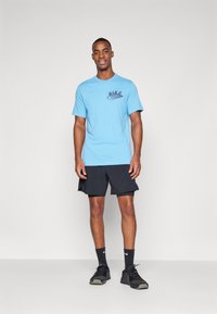 T-shirt in cotone azzurro chiaro con logo Nike nero sul petto, abbinato a pantaloni corti neri e scarpe da ginnastica nere. Design semplice e informale.