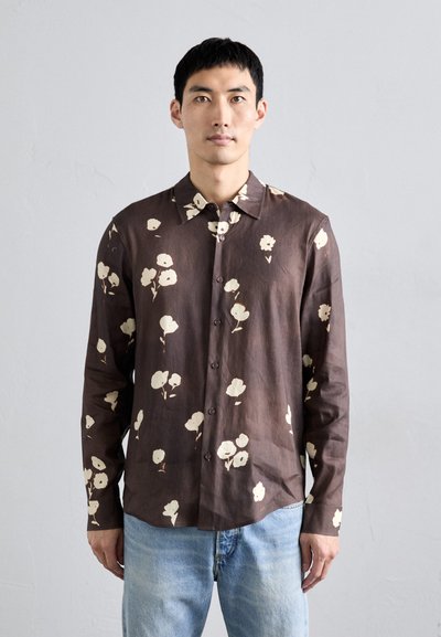 Chemise brune à manches longues avec un motif floral blanc, col boutonné et texture douce, assortie à un jean en denim bleu clair.