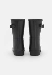 Botas de lluvia de goma negra con una textura lisa, forma rectangular, puntas redondeadas y correas ajustables. Las suelas planas proporcionan estabilidad.