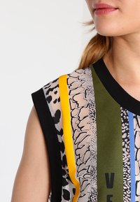T-shirt à manches courtes présentant un mélange d'imprimés animaliers dans des teintes beiges, noirs, verts, jaunes et des rayures bleues, avec un col noir uni.