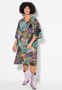 Vestido de estampado paisley colorido con escote en V y mangas anchas, hecho de una tela ligera. Combinado con botas de vaquero brillantes en color lila.