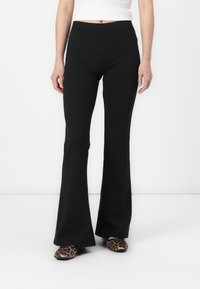 Pantaloni neri a palazzo in tessuto morbido, con un design a vita alta e una vestibilità aderente nella parte superiore. Indossati con scarpe a stampa animale con punta affusolata.