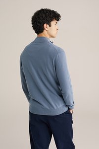 Világoskék kötött pulcsi gallérral, bordázott mandzsettákkal és szegéllyel, tengerészkék nadrággal párosítva. Sima textúra, testhezálló fazon.