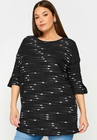 Svartvitt mönstrad oversized topp med korta ärmar, strukturerad tyg och rundad halsringning, som är ihopparad med blå denimjeans.