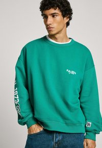 Groene sweatshirt met een ontspannen pasvorm, ronde halslijn en witte logo-details op de borst en de mouw. Gemaakt van zachte, gestructureerde stof.
