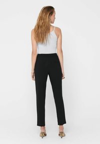 Zwarte getailleerde broek met een elastische tailleband, gecombineerd met een grijze tanktop, vanuit de achterkant getoond. Kenmerkt zich door platte naden en een minimale afwerking.