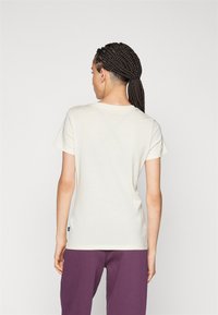 Camiseta de color crema hecha de una tela suave, con un cuello redondo clásico y mangas cortas. Combinada con pantalones morados.