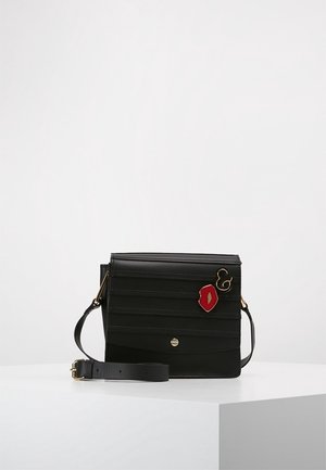 Black leather crossbody bag with adjustable strap and gold-tone hardware, decorated with red lips and ampersand pins on front flap.