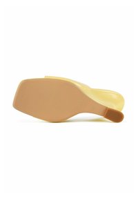 Keltainen liukusandaali, jossa on sileä, kiiltävä pinta ja teksturoitu, beige kumipohja, jossa on vaakasuorat urat pidon parantamiseksi.