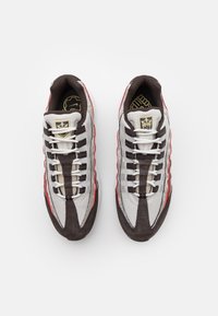 Sneaker mit einem grauen Mesh-Obermaterial, braunen Wildlederakzenten, roten Details und weißen Schnürsenkeln. Logo auf der Zunge und gepolsterter Kragen für mehr Komfort.