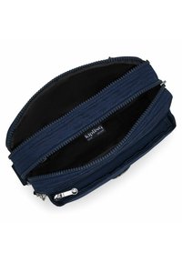 Borsa a tracolla Kipling di colore blu scuro con due scomparti principali aperti e zip in argento su sfondo bianco.