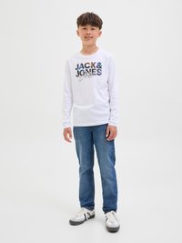 Bijela majica dugih rukava s raznobojnim tekstom "JACK & JONES", u kombinaciji s plavim trapericama i bijelim tenisicama s sivim detaljima. Jednostavan, ležeran izgled.