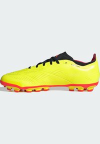 Botas de fútbol de un brillante color amarillo, con una parte superior texturizada, cordones negros y llamativos acentos rojos en la suela y el cuello. Diseñadas para ofrecer tracción.