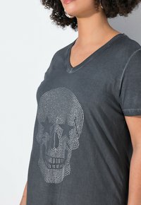 Grå V-udskåret T-shirt lavet af blød bomuld med et blinkende kraniumdesign med stjerneaccents i rhinsten foran.