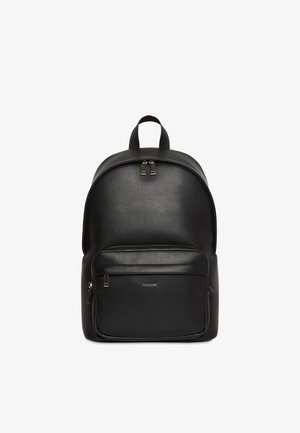 Crni kožnati Calvin Klein ruksak s dvostrukim patentnim zatvaračem, prednjim zip džepom i gornjom ručkom za nošenje.