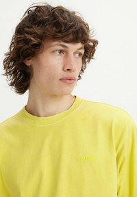 Fluorescent yellow long-sleeve t-shirt with a crew neckline. Features an embroidered Levi's logo in matching yellow on the front.
