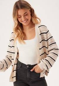 Strick-Cardigan mit offener Struktur in Creme mit schwarzen Streifen. Er hat eine lockere Passform, lange Ärmel und eine Knopfleiste vorne.