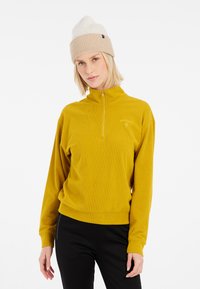 Gelber Reißverschluss-Pullover aus strukturiertem Stoff, mit hohem Kragen und langen Ärmeln. Akzentuiert mit einem kleinen gestickten Logo.