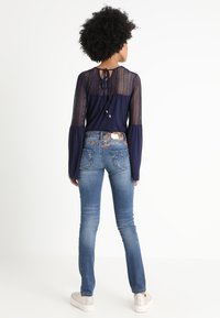 Camiseta de manga larga azul marino con mangas de malla texturizada; combinada con jeans azules desgastados que tienen bolsillos traseros bordados. Zapatillas blancas completan el conjunto.