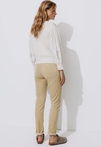 Pull en tricot blanc texturé avec des manches bouffantes brodées, associé à un pantalon en velours côtelé beige et des chaussures à enfiler imprimé léopard. Tenue simple et décontractée.
