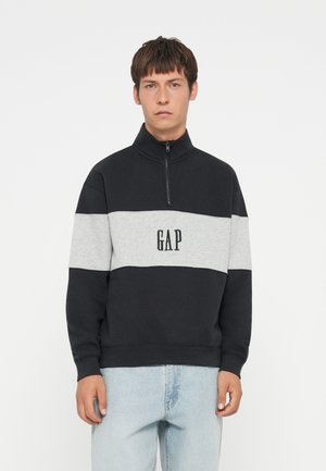 Black and gray color-blocked sweatshirt with a high collar and zipper. Features "GAP" logo in black, designed with a soft, textured fabric.