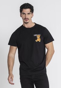 Černé bavlněné tričko s kulatým výst�řihem, krátkými rukávy a grafikou medvěda a textem v oblasti levého prsu.