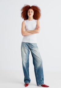 White sleeveless top paired with wide-leg blue jeans. Model wears red pointed-toe heels. Smooth fabric and faded denim texture visible.