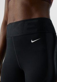 Nahaufnahme einer Person, die schwarze Nike Leggings mit hohem Bund und dem weißen Nike Swoosh-Logo an der Hüfte trägt.