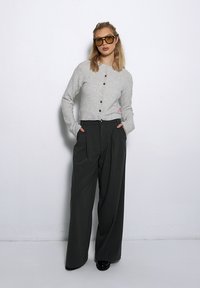 Szary sweter z dzianiny z czarnymi guzikami, połączony z ciemnoszarymi spodniami w kant o wysokim stanie. Modelka nosi oversize'owe okulary przeciwsłoneczne.