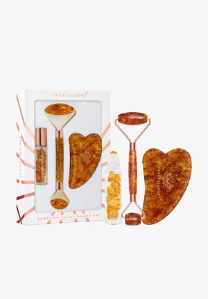 Zestaw do pielęgnacji twarzy z kamieni szlachetnych, zawierający wałek i gua sha w odcieniach bursztynu, z akcentem w kolorze różowego złota. Zawiera szklaną fiolkę z kryształami.