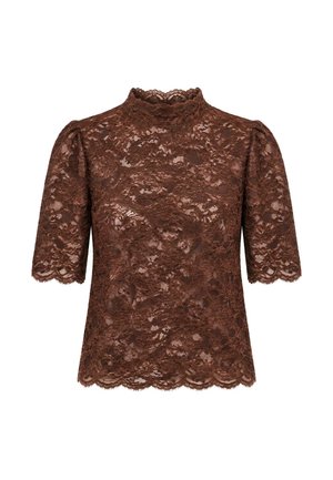 Femme portant un haut court en dentelle marron, un pantalon droit crème et des mocassins crème, debout devant un fond clair uni.