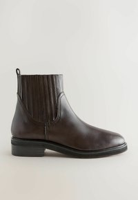 Bottine en cuir marron avec des panneaux élastiques sur les côtés et une languette. Texture lisse, bout arrondi et semelle en caoutchouc plate. Design minimaliste.