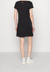 Czarna sukienka o krótkim rękawie i luźnym kroju, z tylnym logo, gładką teksturą oraz długością do kolan. Noszona z białymi trampkami.