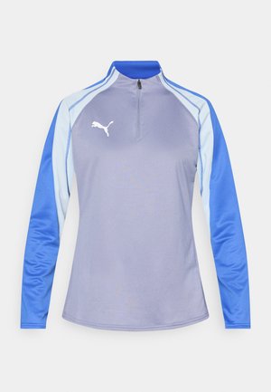 Długi rękaw sportowej bluzki w jasnym fiolecie z niebieskimi akcentami. Posiada półzamknięty kołnierz i białe logo Puma na piersi. Gładka faktura.
