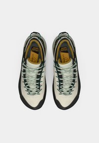 Zapatos de escalada de color gris claro con un upper texturizado, suela de goma oscura, un sistema de cordones intrincado y plantilla contrastante amarilla.