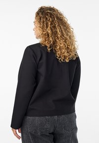 Svart långärmad topp med avslappnad passform, med rundad halsringning och enkel design. Matcher med mörkgrå jeans. Texturerat, mjukt material.