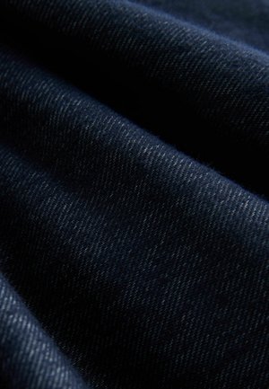 Mörkt denimtyg med fin twillväv. Har en djup marinblå färg och subtil textur med ljus sömnad synlig längs kanterna.