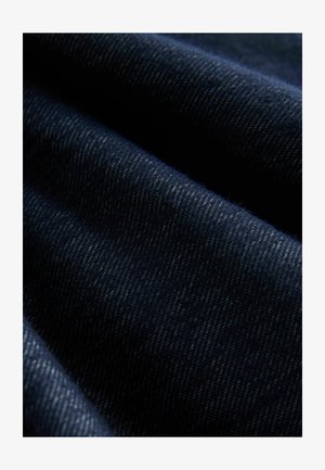 Mörkt denimtyg med fin twillväv. Har en djup marinblå färg och subtil textur med ljus sömnad synlig längs kanterna.