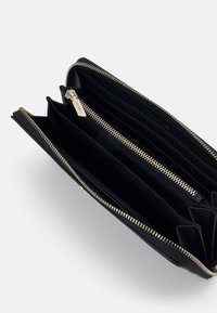 Portafoglio nero realizzato in materiale texturizzato con zip dorate, dotato di più scomparti e slot per carte per una migliore organizzazione.