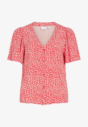 Bluza coral roz cu mâneci scurte, buline albe neregulate, decolteu în V, nasturi în față și umeri ușor bufanți.