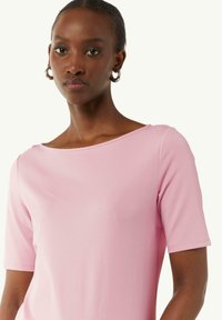 Helles Pink, kurzärmliges Oberteil mit einem Bootsausschnitt, aus einem glatten Stoff; zeichnet sich durch klare Linien und eine taillierte Silhouette aus.
