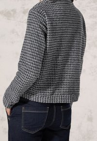 Gray textured jacket with a houndstooth pattern, featuring a collar and ribbed hem, paired with dark blue jeans.