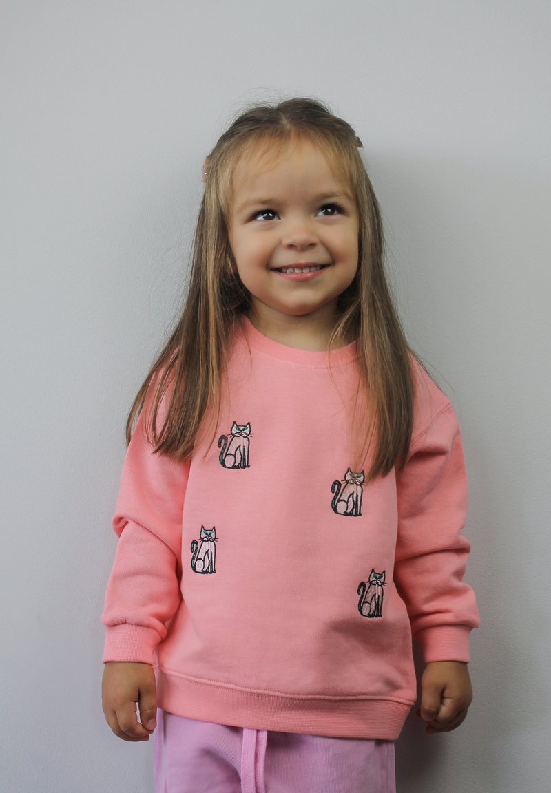Felpa rosa con maniche lunghe, caratterizzata da ricami di gatti. Tessuto morbido e scollatura tonda, abbinata a pantaloni rosa chiaro.
