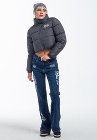 Cropped black puffer jacket with high collar and front zipper, paired with flared blue jeans featuring white embroidered designs.