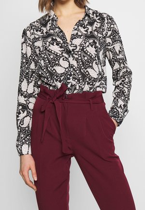 Blusa a maniche lunghe in bianco e nero con un colletto, caratterizzata da motivi floreali. Abbinata a pantaloni bordeaux a vita alta con una cintura legata.