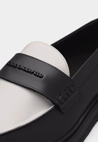 Μοκασίνι από δέρμα σε ασπρόμαυρο, με μαύρο λουράκι στο μπροστινό μέρος, χαραγμένο με το λογότυπο "KARL LAGERFELD".