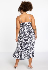 Ärmelloses Midi-Kleid in Weiß mit schwarzem abstraktem Muster. Verfügt über Rüschen am Saum und verstellbare Spaghetti-Träger. Glatte Stofftextur.