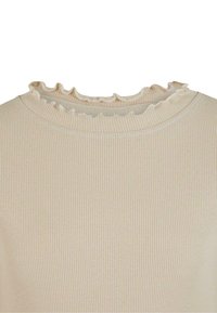 Krēmkrāsas ribots adīts tops ar volānu apmalu pie apaļās kakla līnijas, kas parāda detalizētu apkakles tekstūru un auduma rakstu.