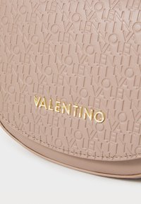 Borsa a tracolla in pelle beige con motivo a logo "Valentino" in rilievo e hardware dorato. Texture liscia con forma rotonda e dettagli cuciti.